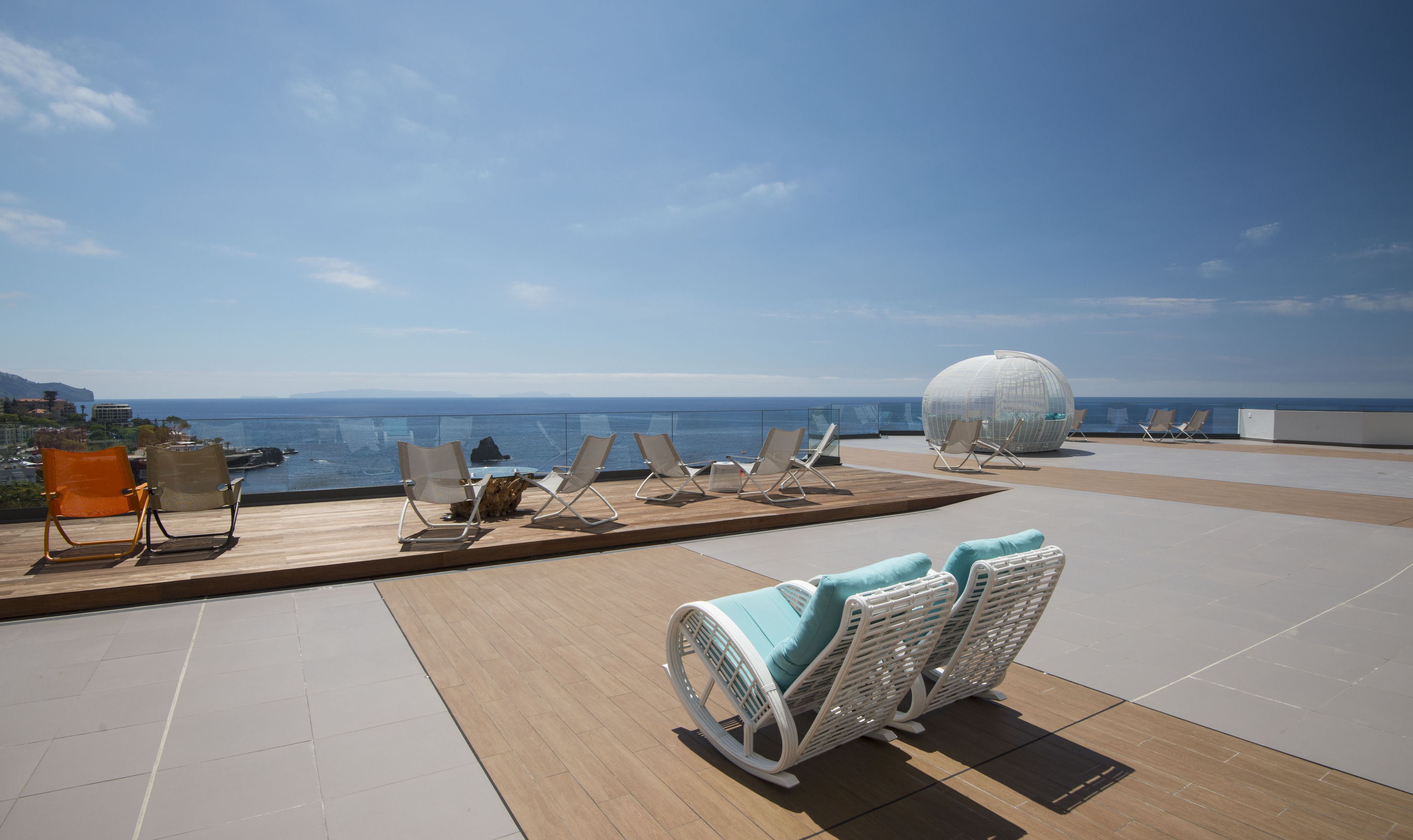 Een terras op het dak met een panoramisch uitzicht over de oceaan, ingericht met diverse zitplaatsen, waaronder lounge fauteuils en een bolvormige zithoek.