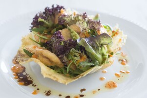 A plate of food with various greens, a crispy element, and sauce.