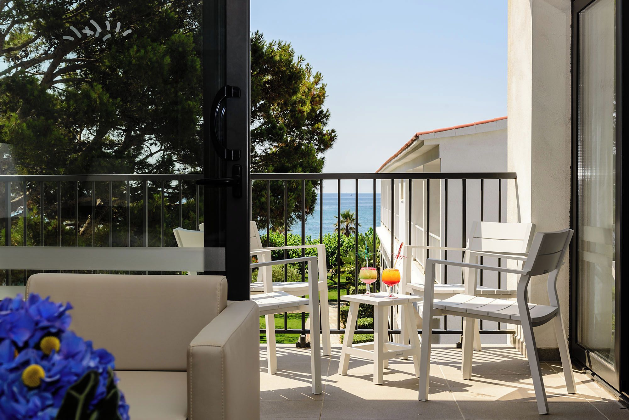 Un balcón con muebles blancos, un ventanal de vidrio y vista al mar.