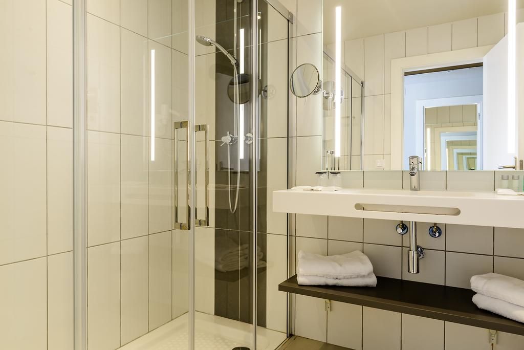 Een moderne badkamer met een douchecabine van glas, een witte wastafel met spiegel, en netjes opgevouwen handdoeken op een plank.