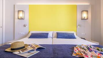 Una cama doble con dos almohadas, un sombrero, una revista y un textil colorido sobre la colcha.