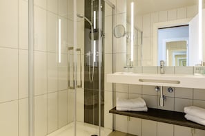 A modern bathroom with a glass-enclosed shower, a white sink with a mirror above it, and neatly folded towels on a shelf. - Estival Eldorado (Cambrils)
