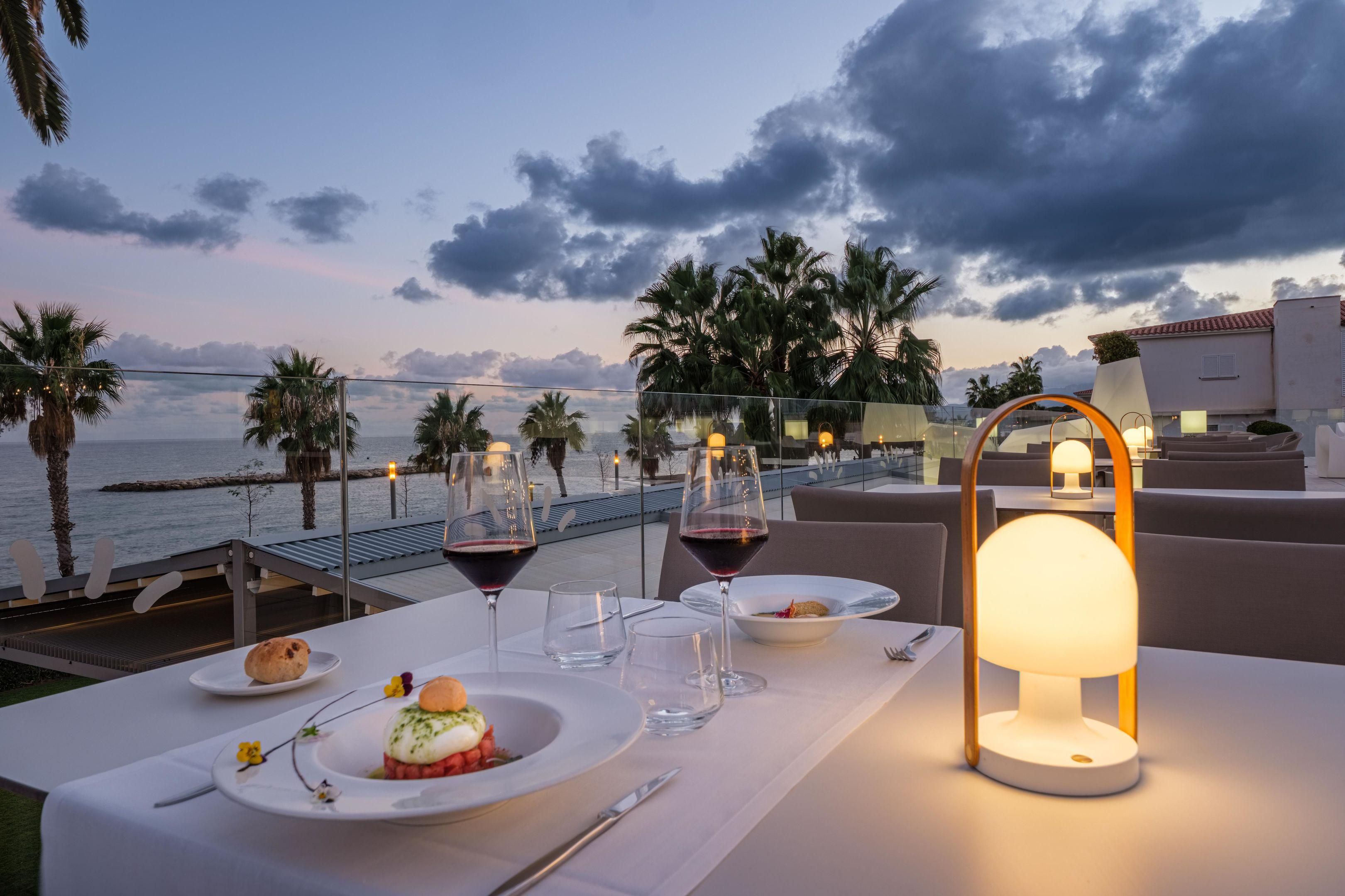 A table set for a meal with a view of the sea and palm trees.