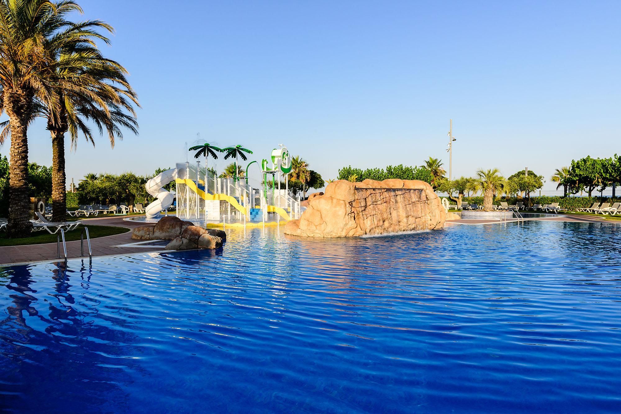 Une piscine avec un toboggan, des palmiers et des chaises longues.
