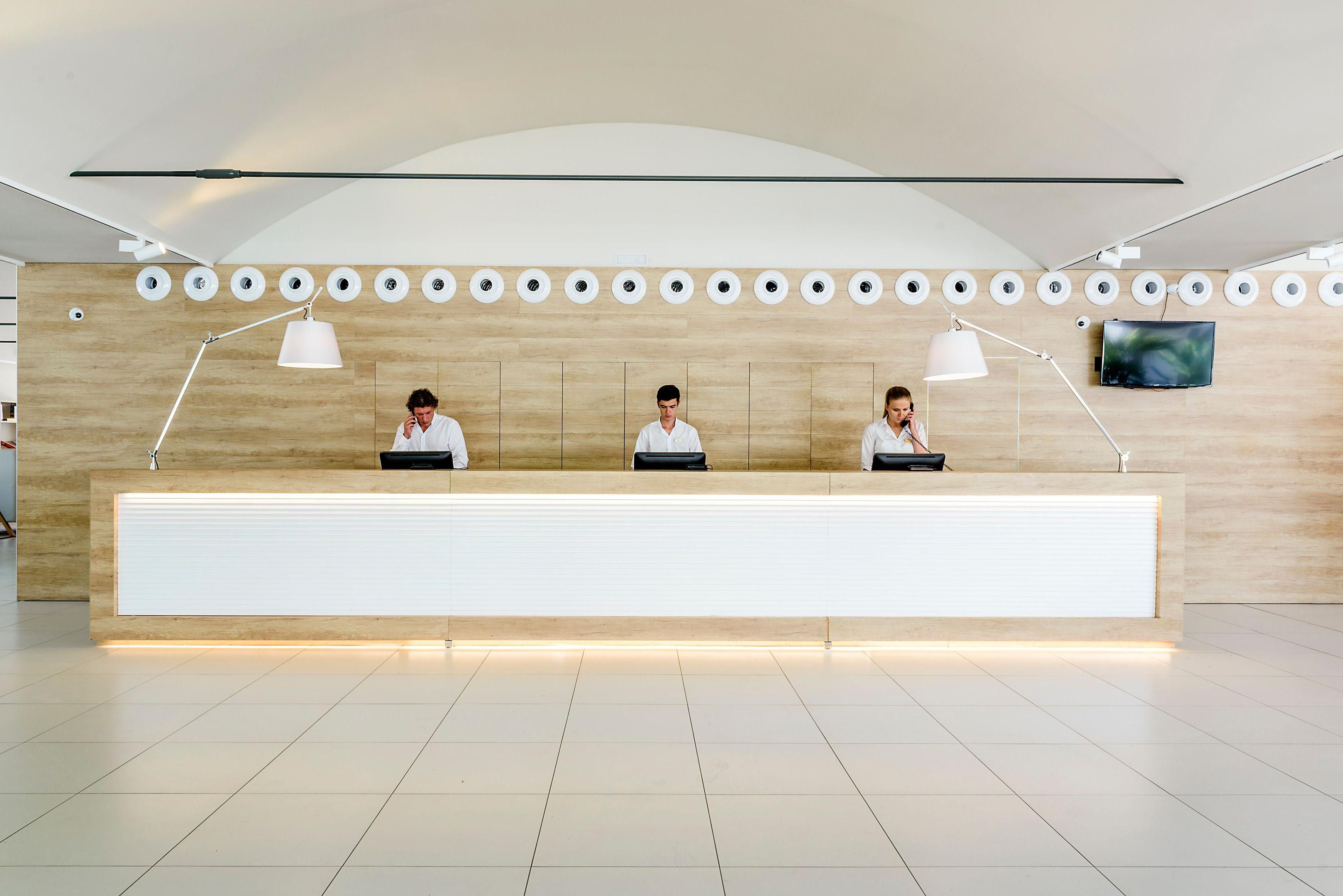 A reception desk with three staff members, a modern design, and a flat-screen TV on the wall.