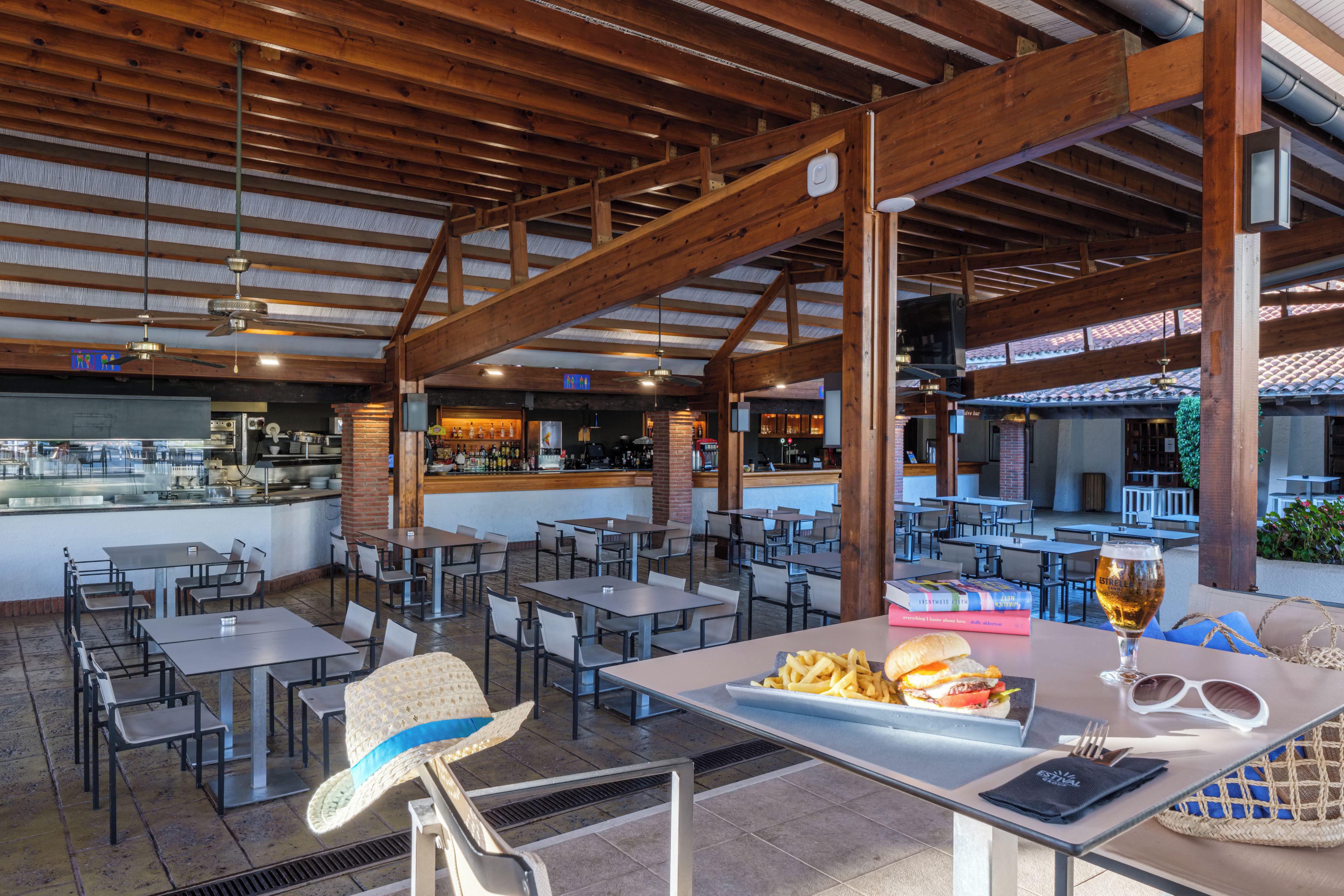 A spacious outdoor dining area with multiple tables and chairs, a bar area, and a view of the surrounding landscape.