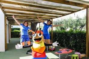 A covered outdoor area with a wooden structure, a large mascot figure, and children's play equipment. - Estival Eldorado (Cambrils)