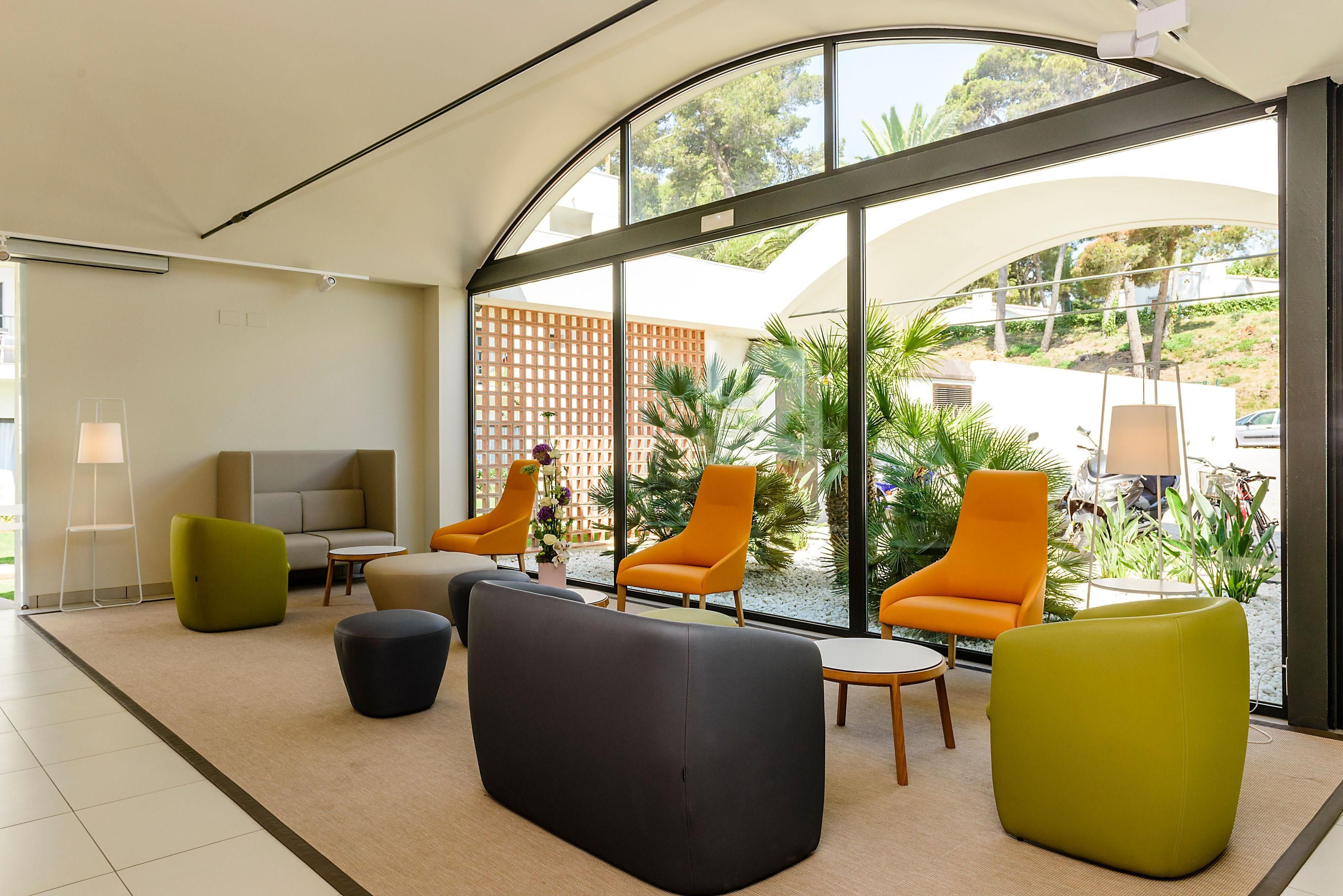 Un interior moderno con techo curvo, ventanas amplias y una zona de estar con sillas naranjas y verdes.