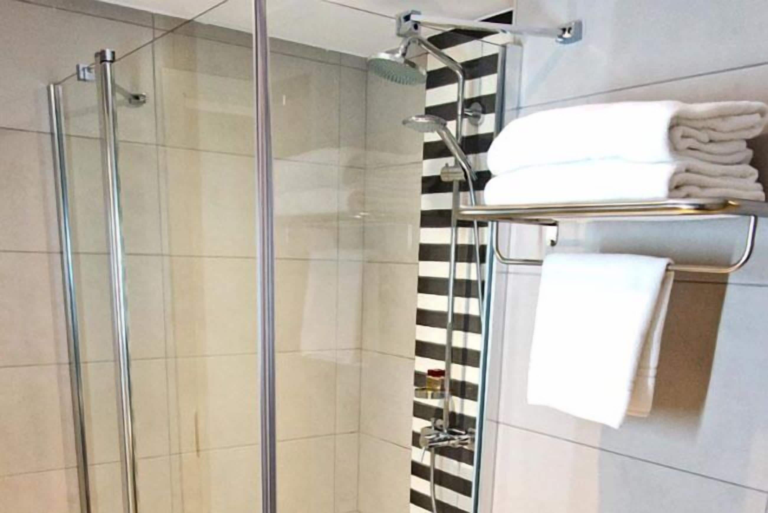 Un baño moderno con ducha envuelta en vidrio, diseño de pared a rayas y un perchero con toallas dobladas prolijamente.