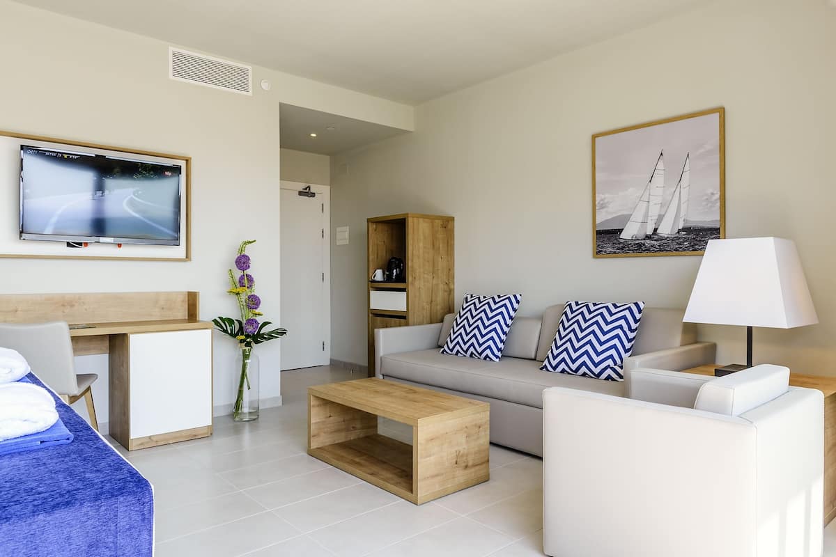 A modern living room with a sofa, coffee table, TV, and a painting of sailboats.