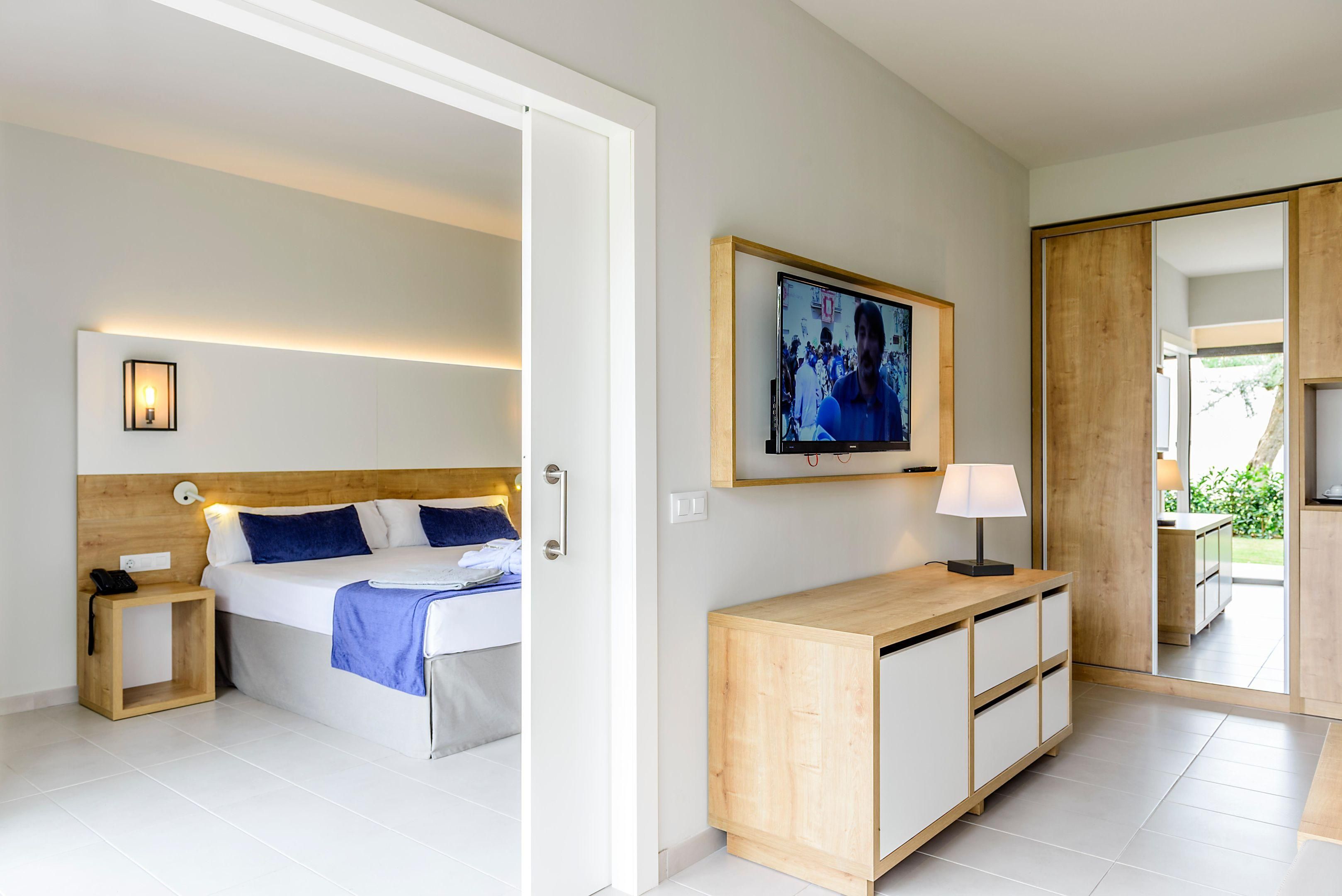 A modern hotel room with a bed, bedside table, lamp, and a painting on the wall.