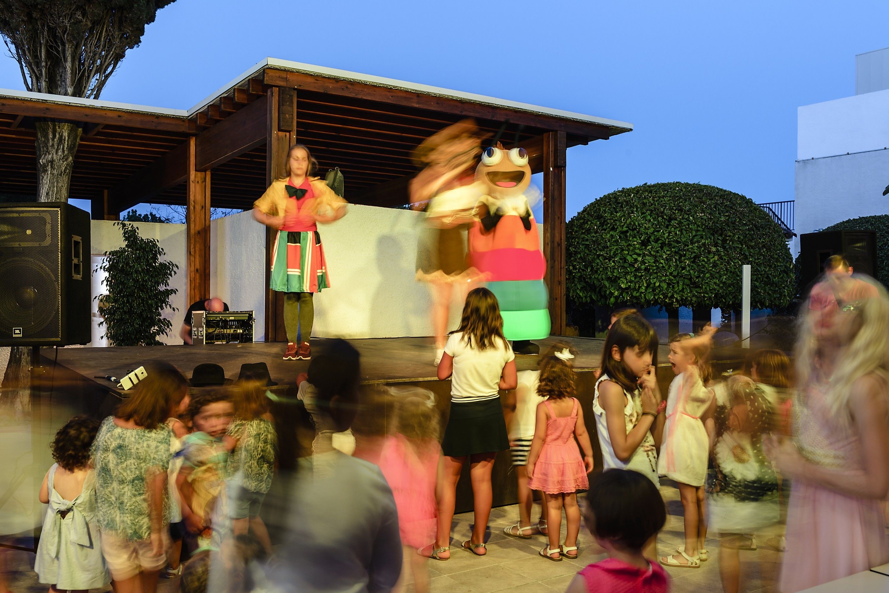 A stage with a performer and a puppet, surrounded by an audience.