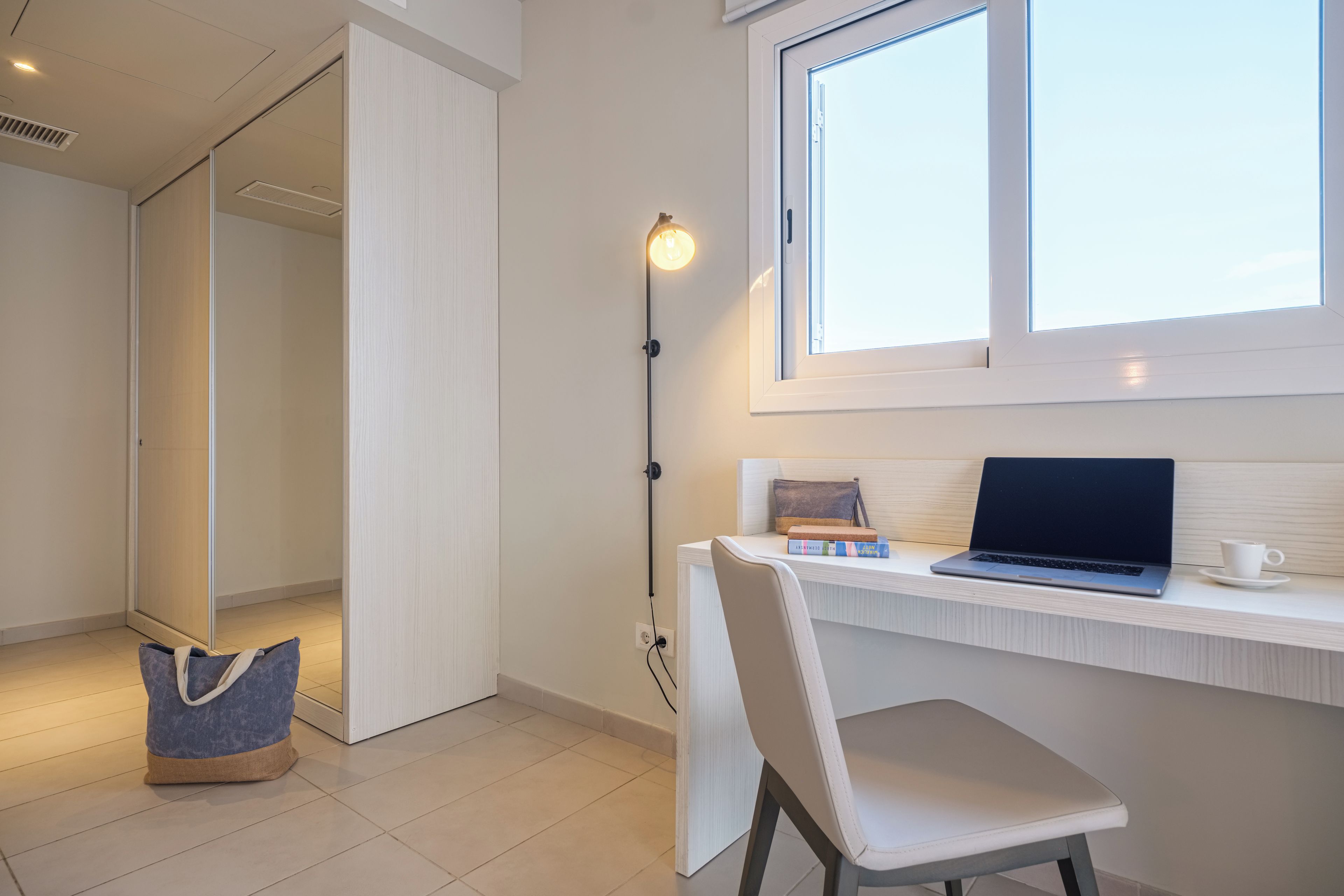 Ein modernes Zimmer mit Schreibtisch, Stuhl, Laptop und Fenster.