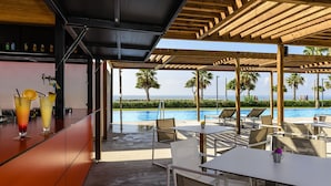 Eine Poolbar mit Getränken, Sitzgelegenheiten im Freien und Blick auf Pool und Meer.