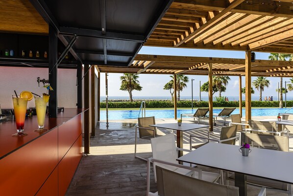 A poolside bar with drinks, outdoor seating, and a view of the pool and ocean. - Estival Eldorado (Cambrils)