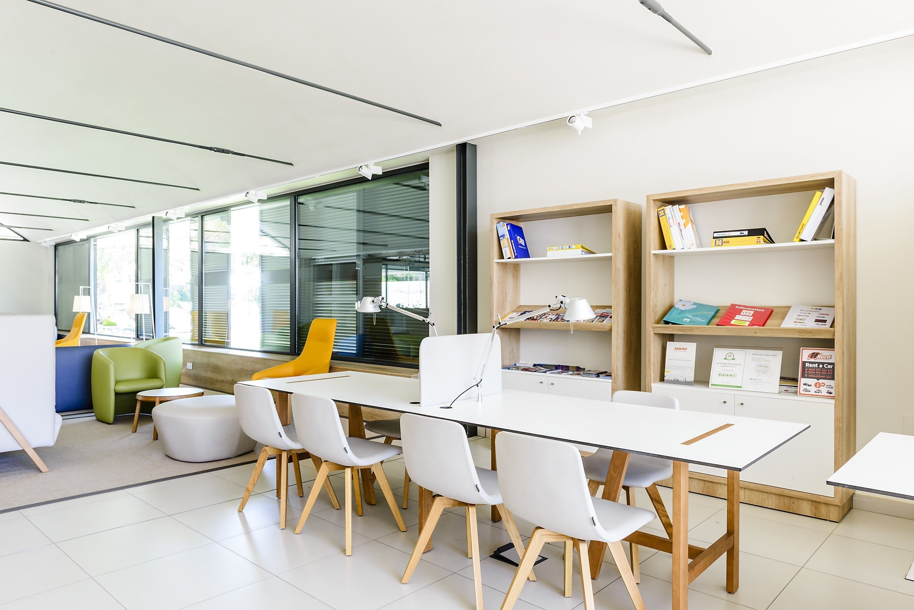 A modern library with a long table, white chairs, and bookshelves.