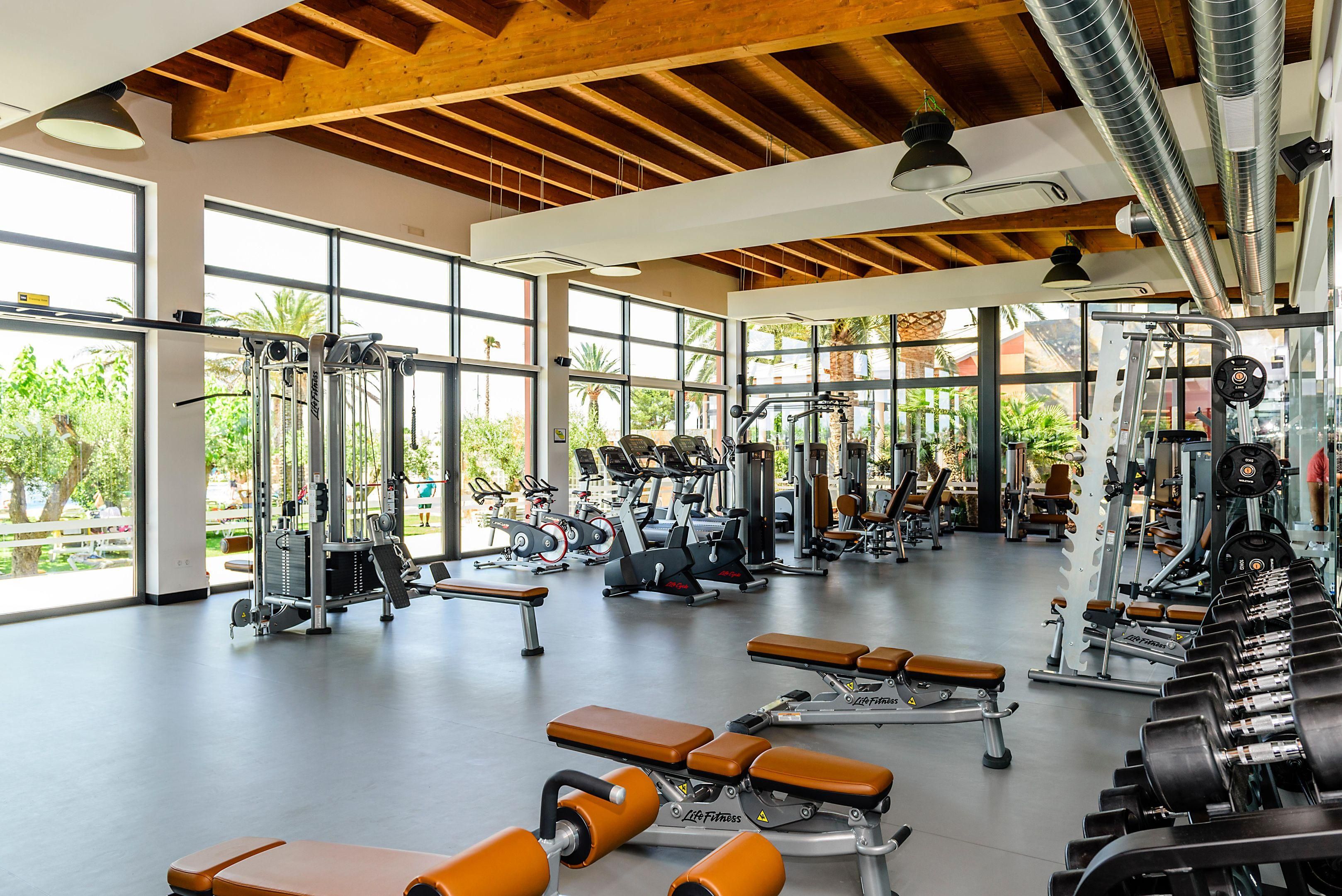 A spacious gym with various exercise equipment, large windows, and a wooden ceiling.