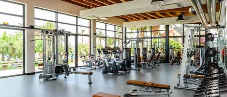A spacious gym with various exercise equipment, large windows, and a wooden ceiling.