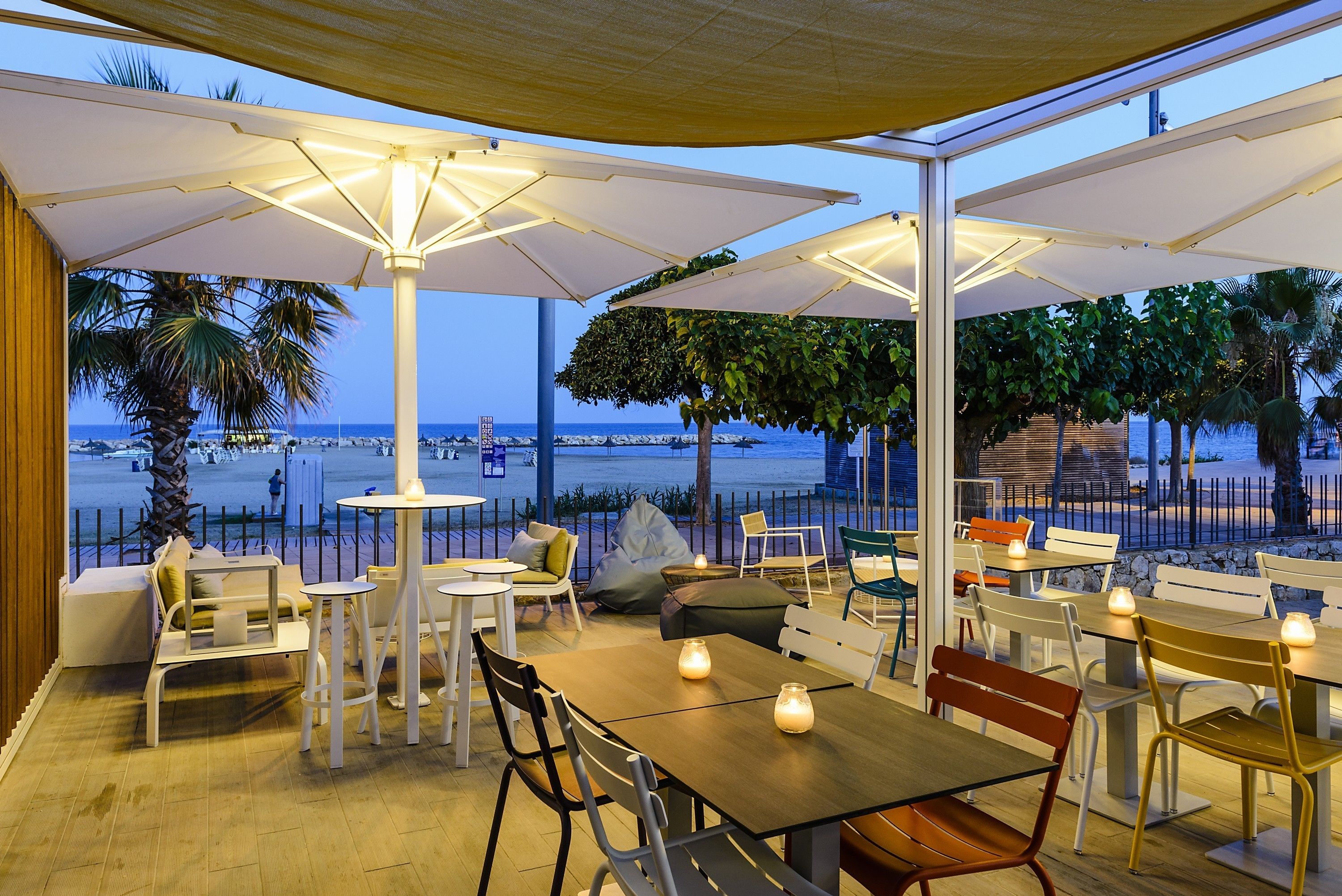 Een terras met tafels, stoelen en parasols, met uitzicht op het strand.