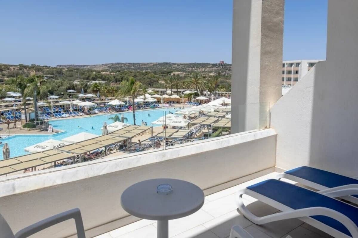 A balcony with a pool view, lounge chairs, and a table.