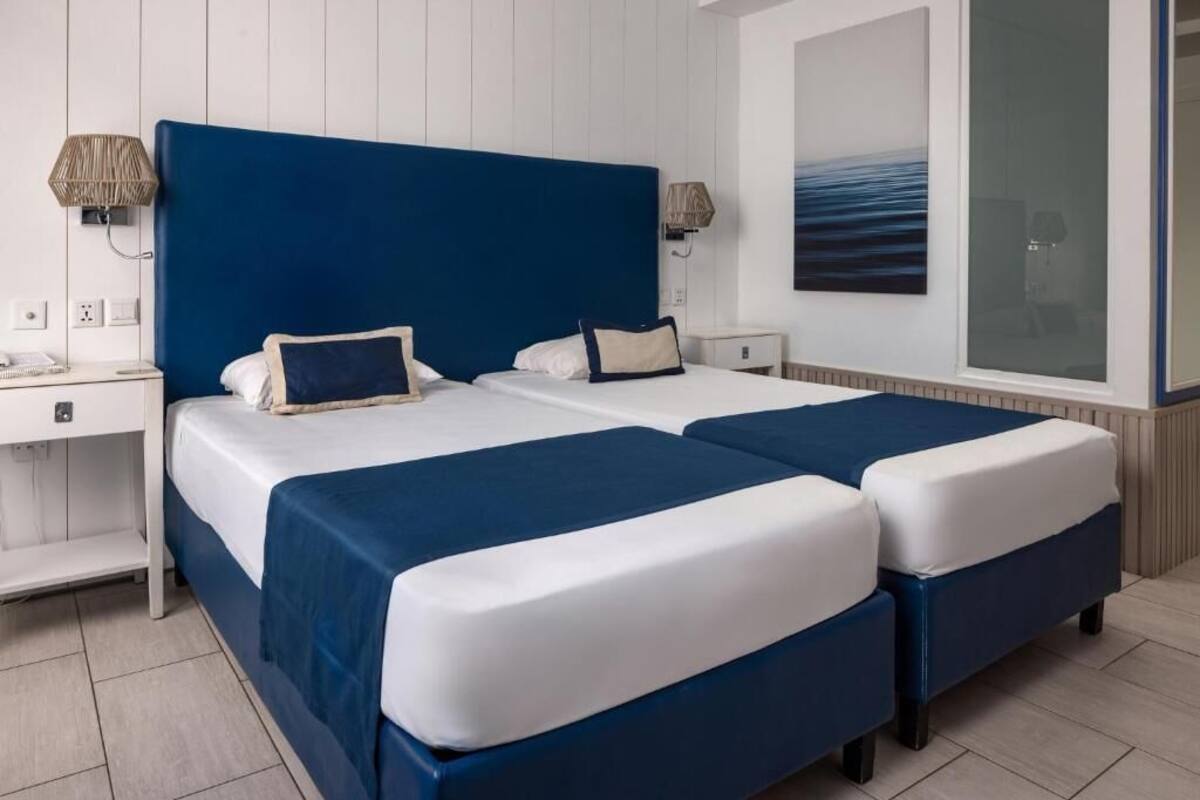 A double bed with a blue headboard, two bedside tables, and a large window with a view of the sea.