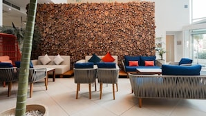 A modern lounge area with sofas and chairs, a wooden log wall, and a large window. - db Seabank Resort and Spa (Mellieha)