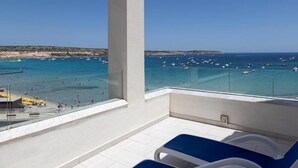 A balcony with a clear view of the sea, lounge chairs, and a tiled floor. - db Seabank Resort and Spa (Mellieha)