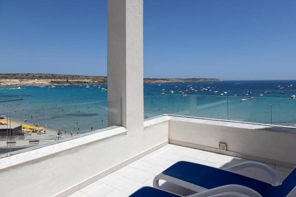 A balcony with a clear view of the sea, lounge chairs, and a tiled floor.