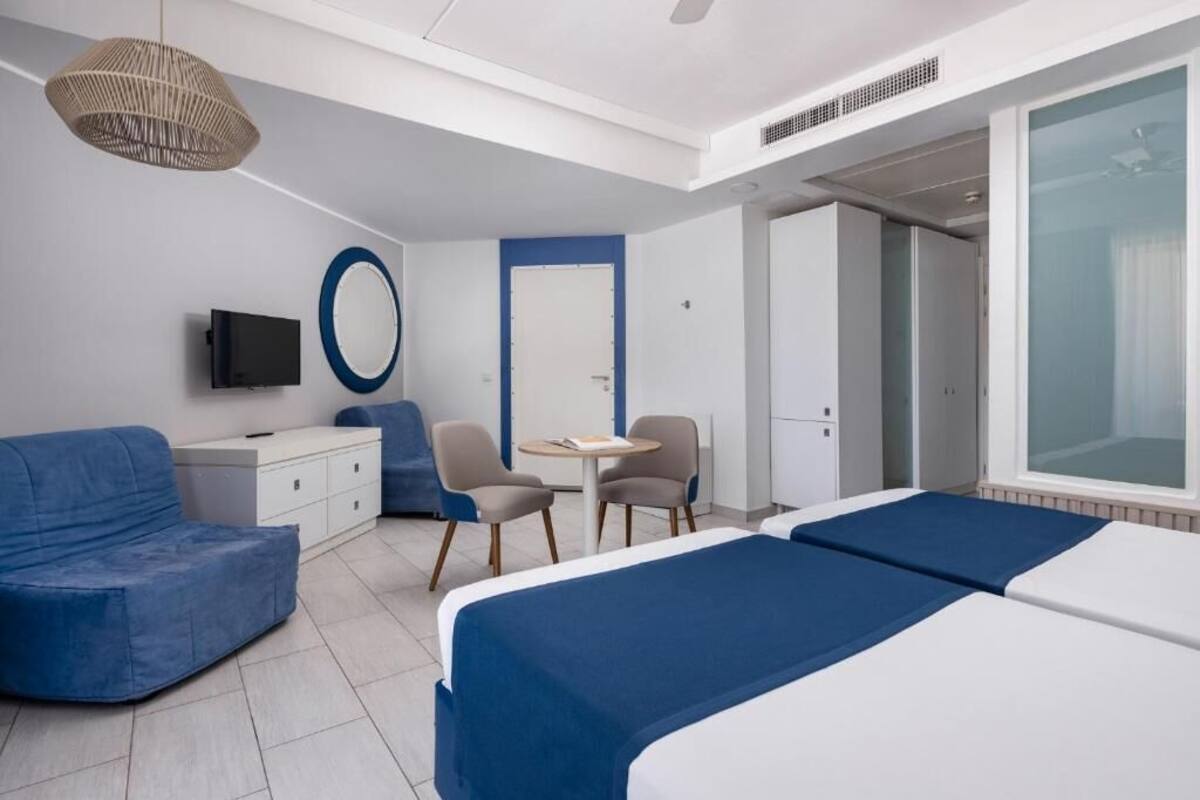 A modern hotel room with a bed, a sofa, a desk, and a TV.