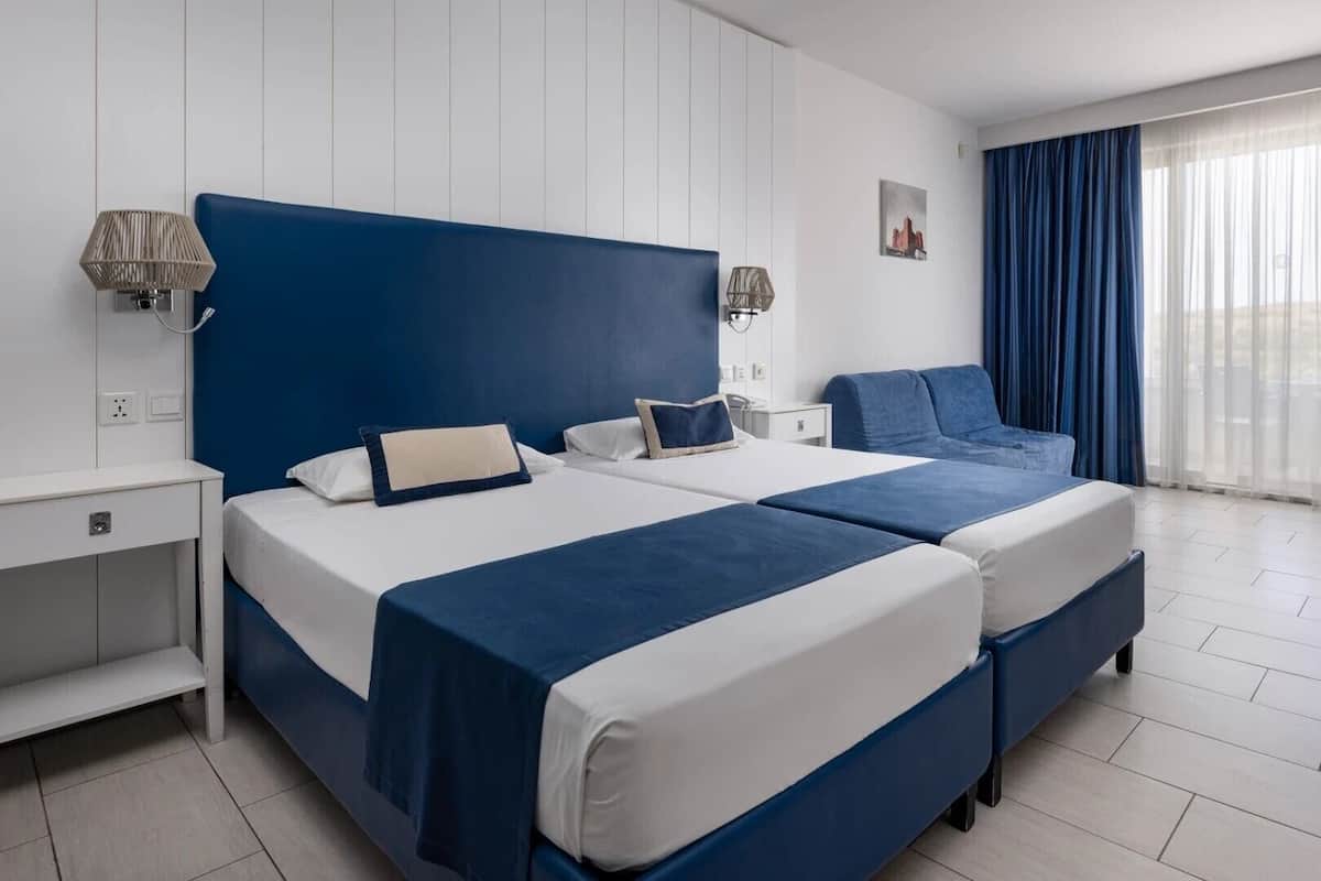 A hotel room with two beds, a desk, and a window with curtains.