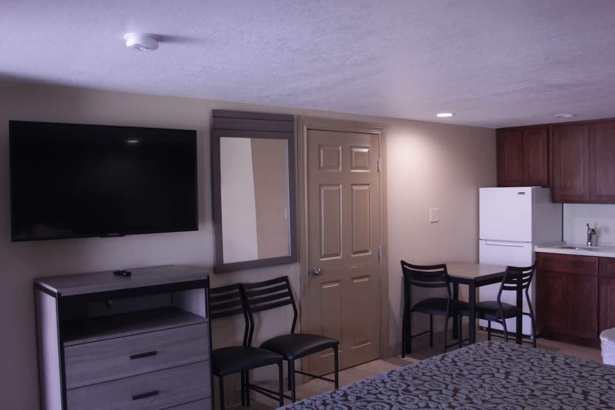 Une chambre d’hôtel compacte comprenant un lit, un bureau avec une chaise, une télévision, un réfrigérateur et une petite kitchenette.
