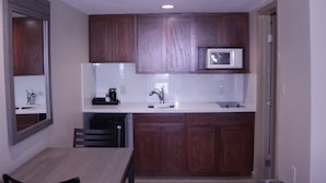 A compact kitchen with wooden cabinets, a microwave, a sink, and a dining table. - Americas Best Value Inn Port Aransas (Port Aransas)