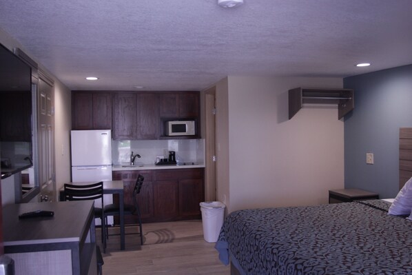 A compact hotel room with a kitchenette, a bed, a desk, and a chair.