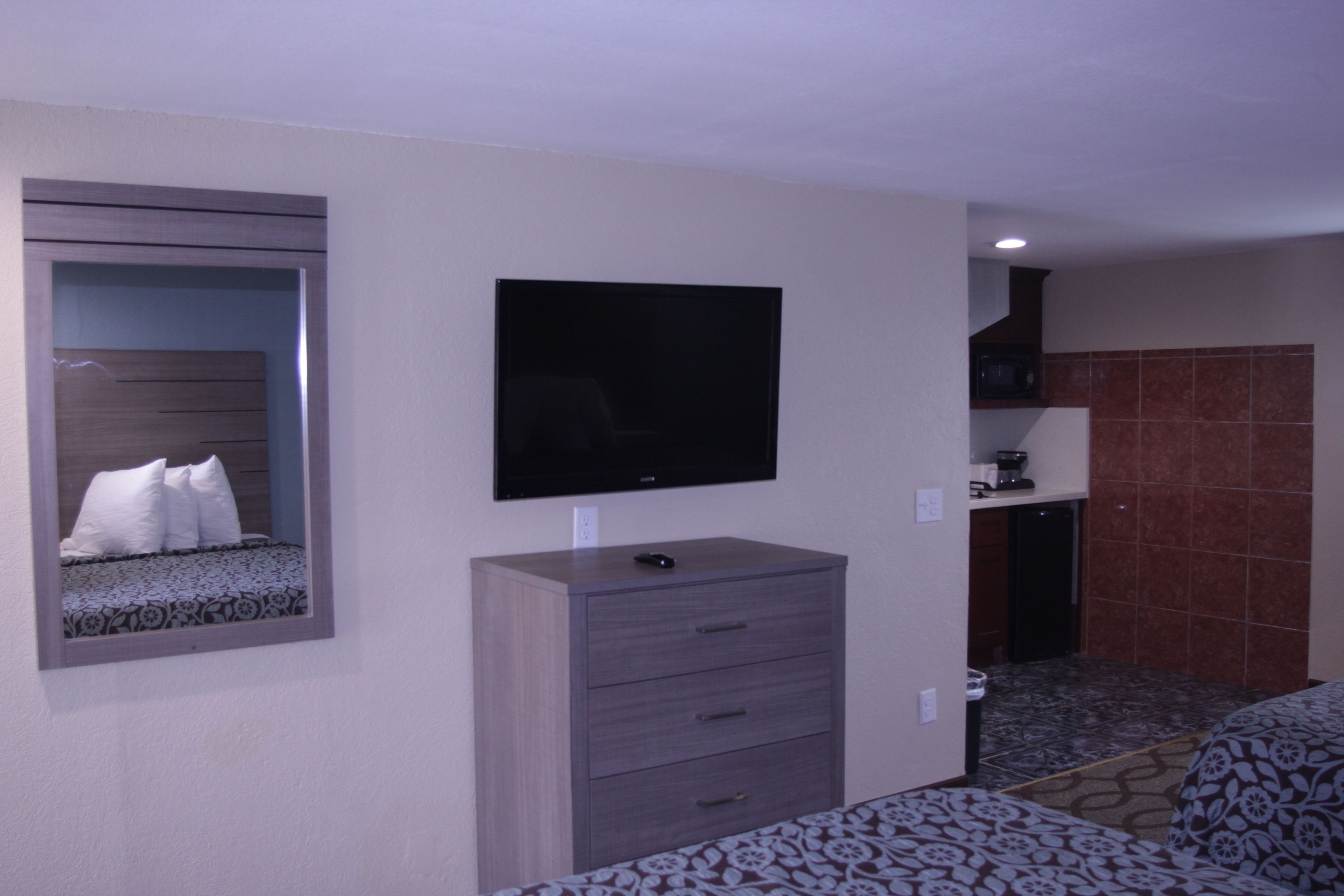 Een hotelkamer met een bed, een dressoir, een aan de muur bevestigde televisie en een kitchenette.