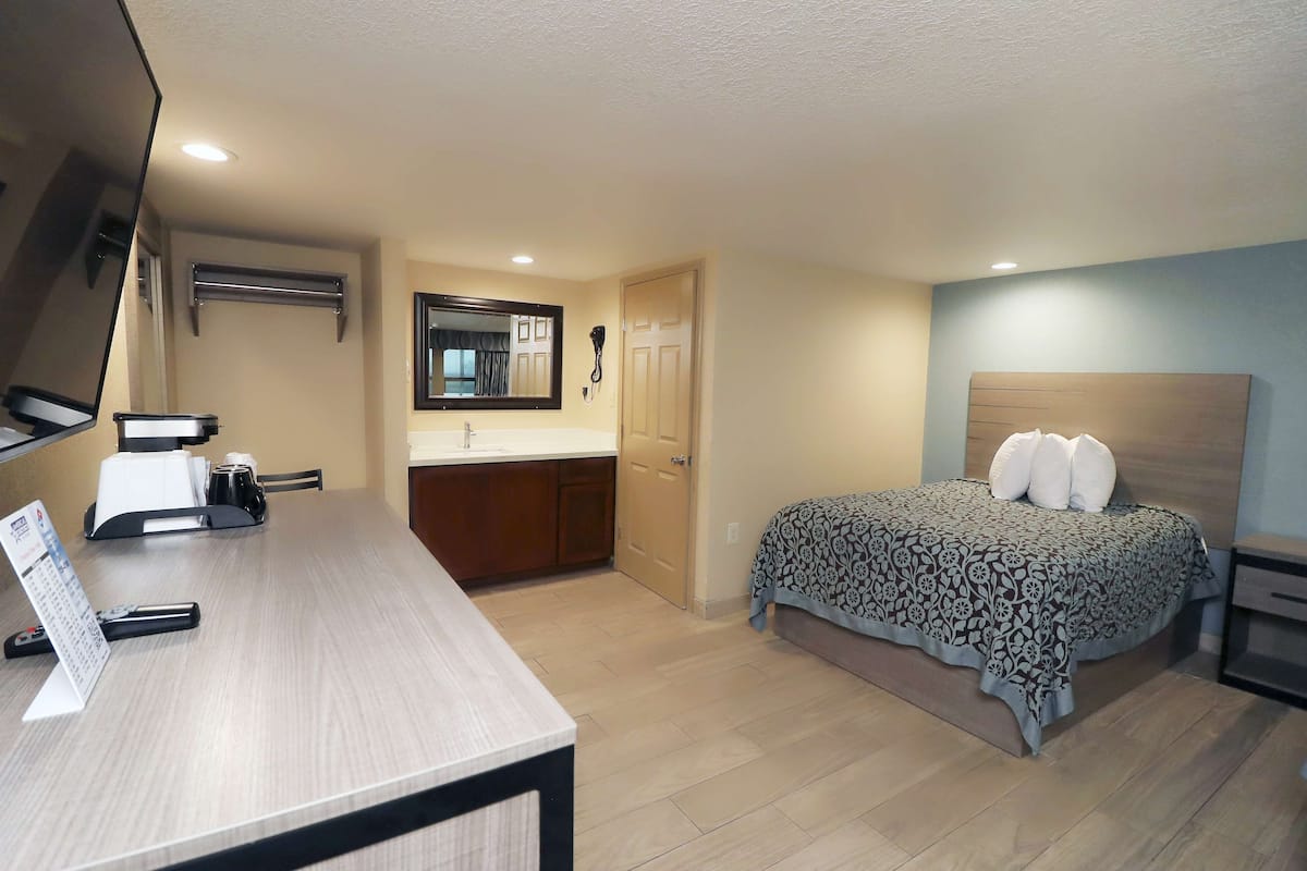 Une chambre d’hôtel comprenant un lit, un bureau avec un téléphone, un miroir et une salle de bain avec un lavabo et des toilettes.