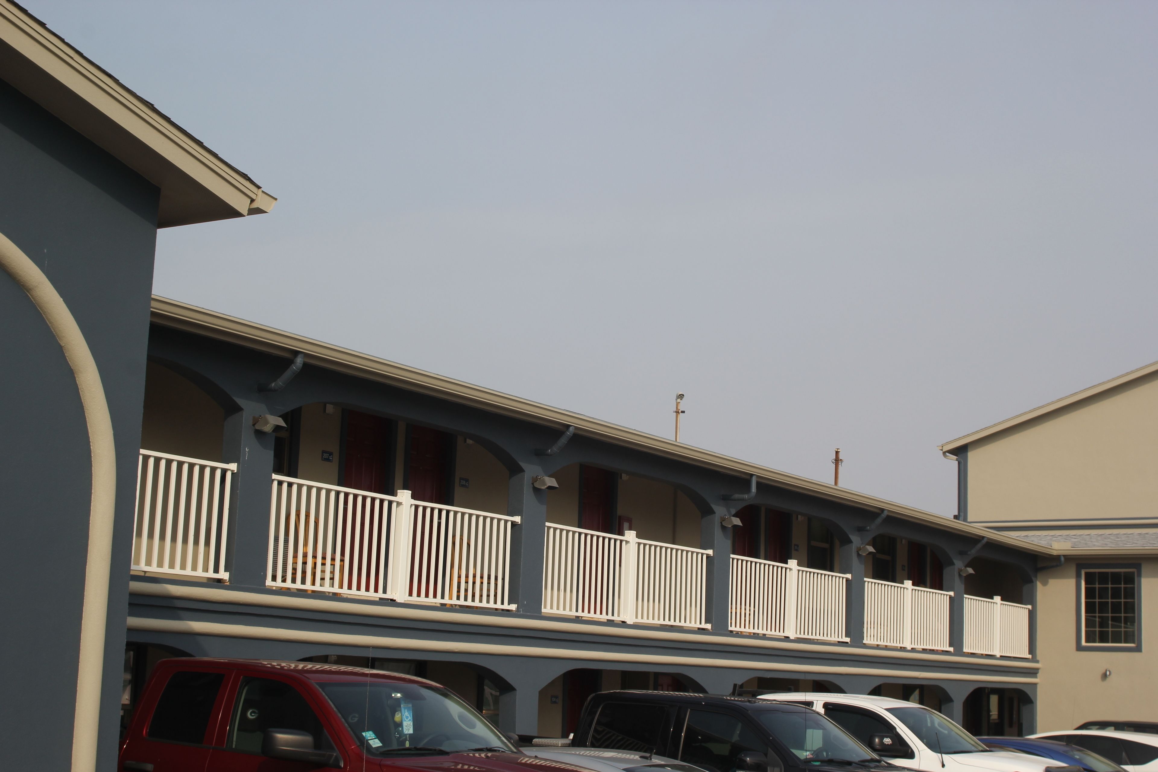 A multi-story building with balconies, a parking lot with several cars, and a clear sky.