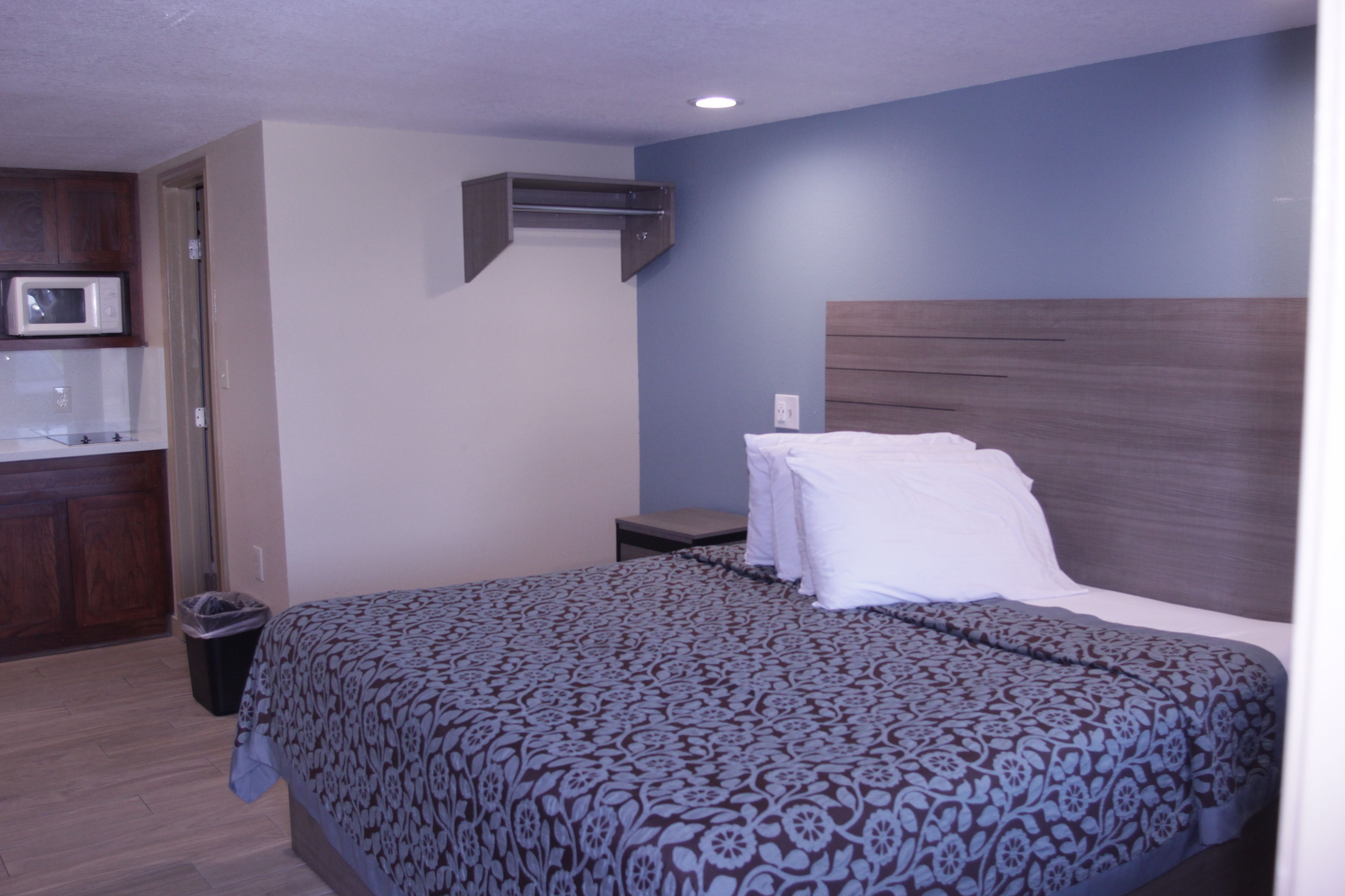 A hotel room with a bed, a bedside table, a microwave, and a trash bin.