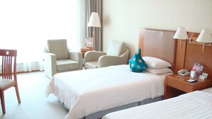 Une chambre d’hôtel avec deux lits, une chaise, une table de chevet avec une lampe et une fenêtre avec des rideaux.