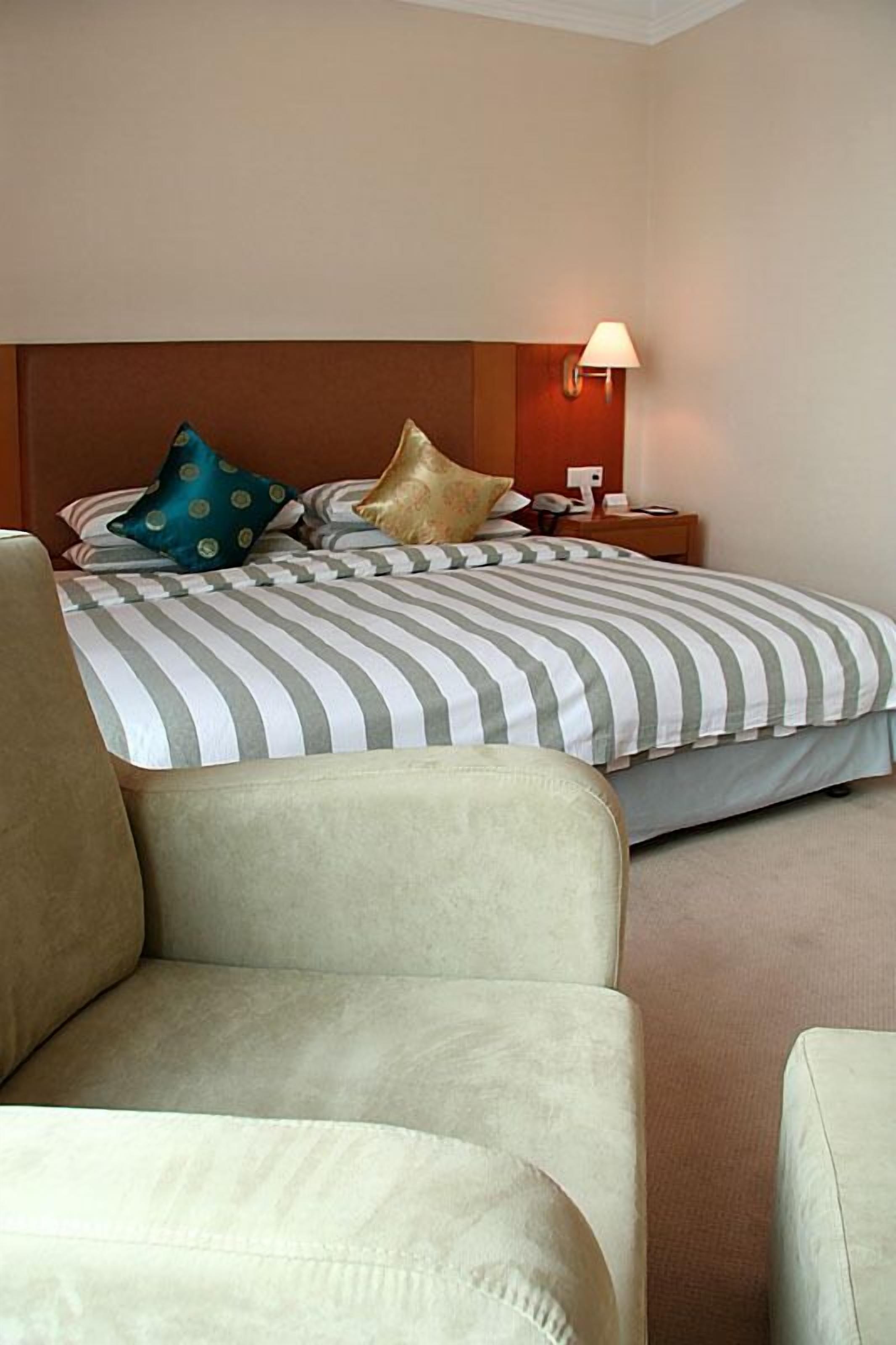 A hotel room with a bed, a nightstand, a lamp, and a chair.