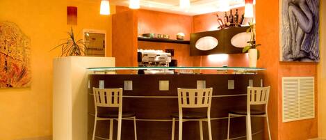A bar area with a glass counter, three white bar stools, and overhead pendant lighting.