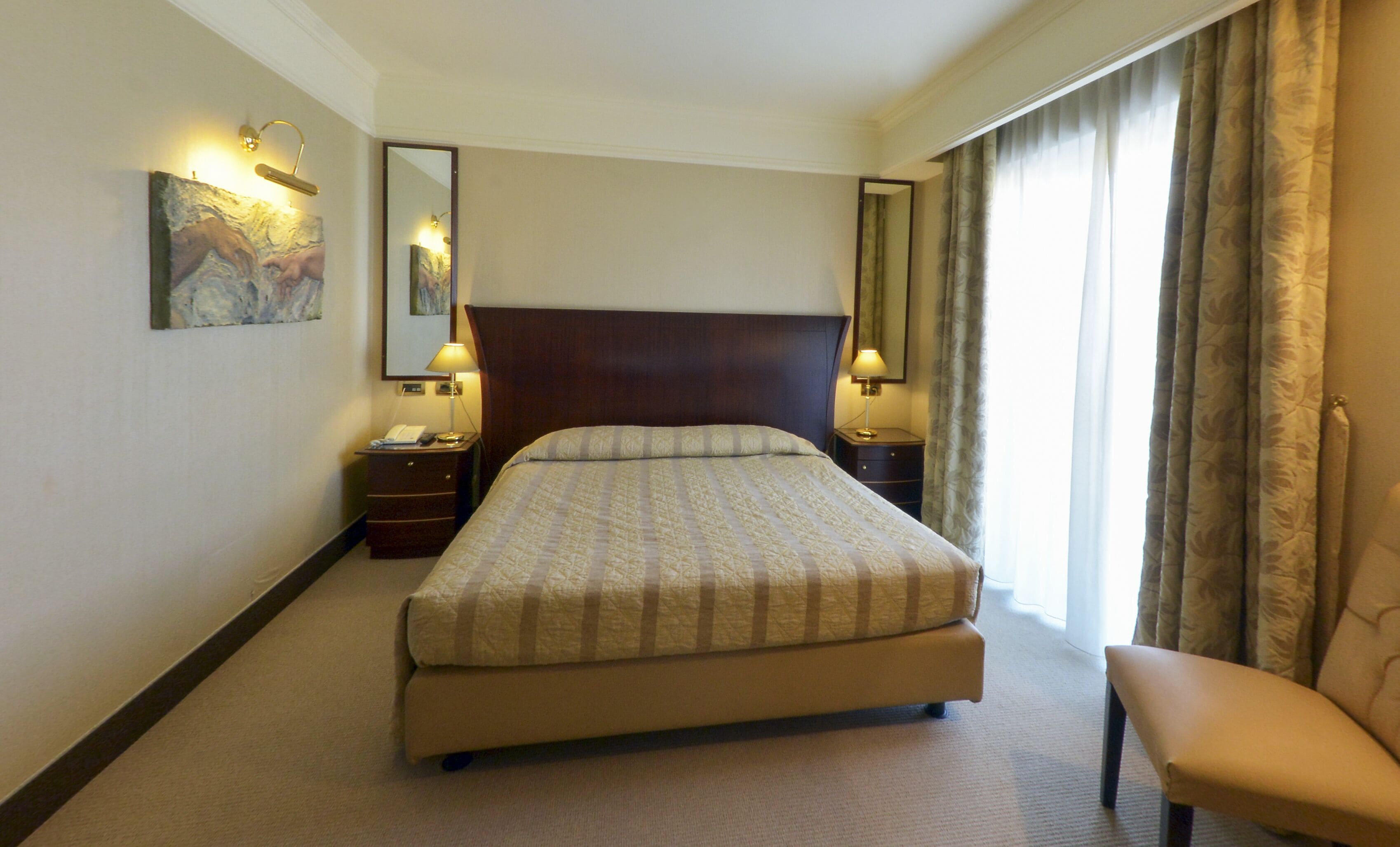 A hotel room with a large bed, two bedside tables with lamps, a chair, and a painting on the wall.