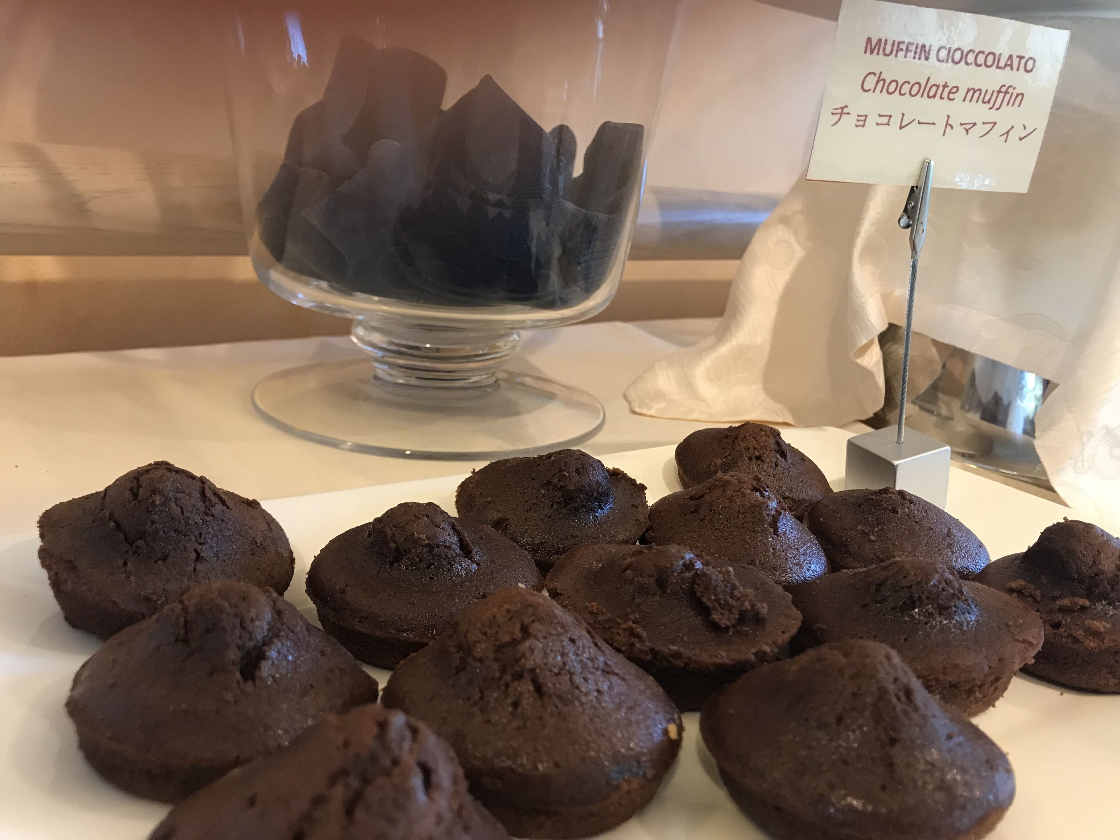 A display of chocolate muffins with a sign indicating they are 'MUFFIN CICCOLATO Chocolate muffin'.