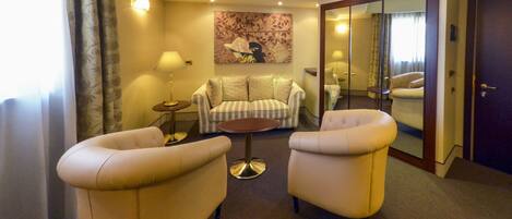 A hotel room with a sofa, two armchairs, a small round table, a lamp, and a painting on the wall.