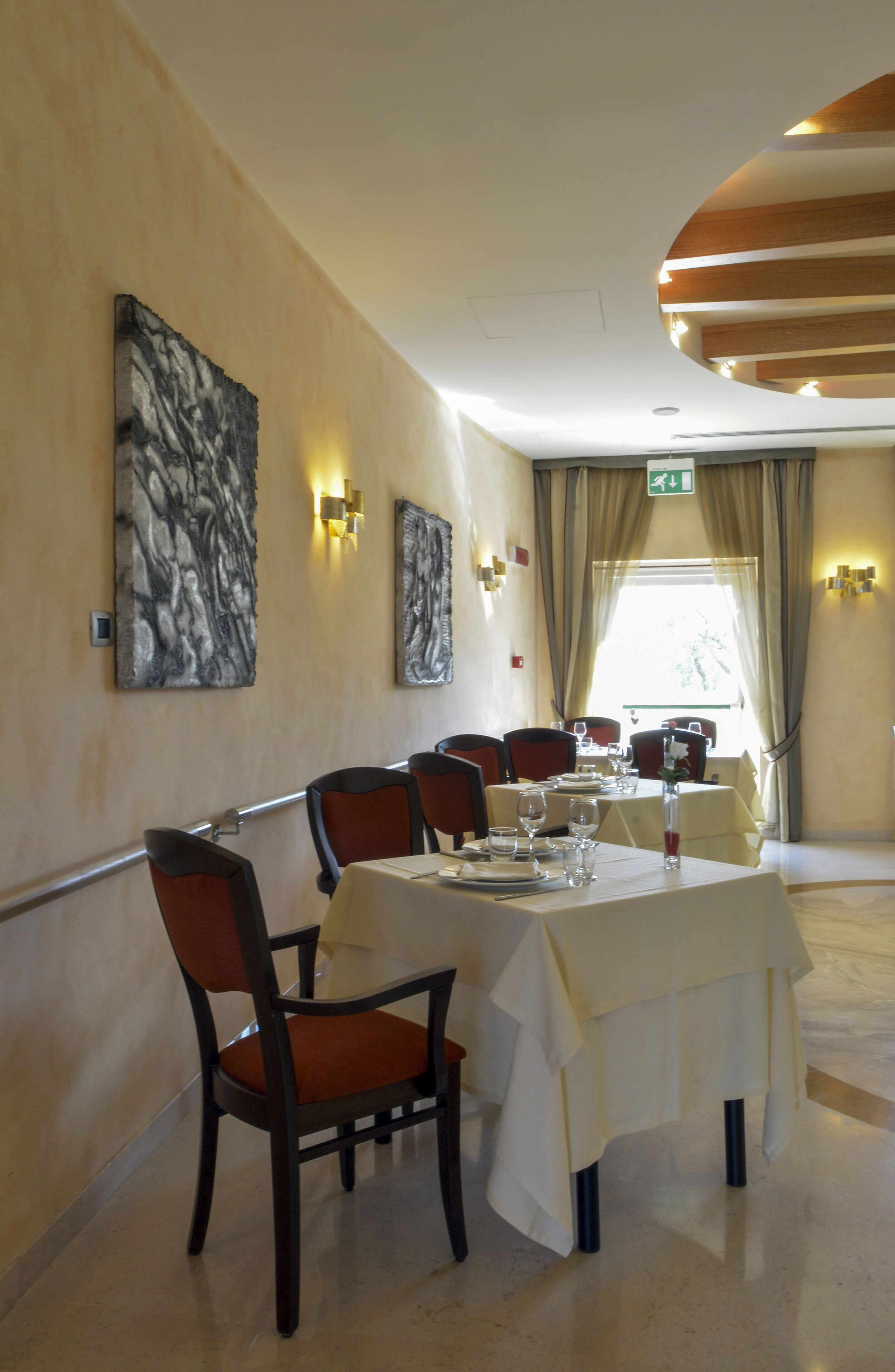 A dining area with a table set for four, surrounded by chairs, with artwork on the walls and a window with curtains.