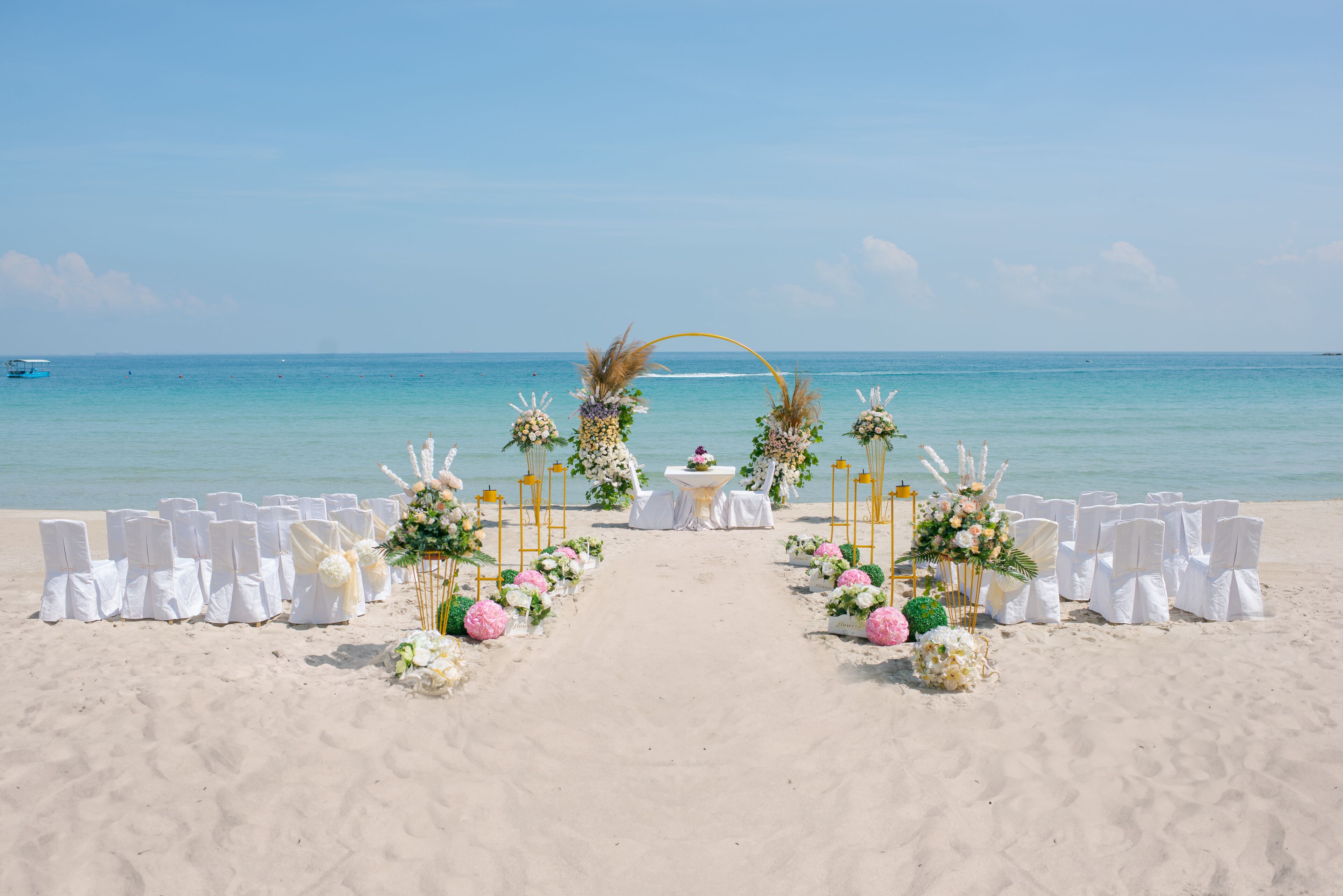 Une cérémonie de mariage organisée sur la plage, avec une allée blanche, des décorations florales et une table placée au centre.