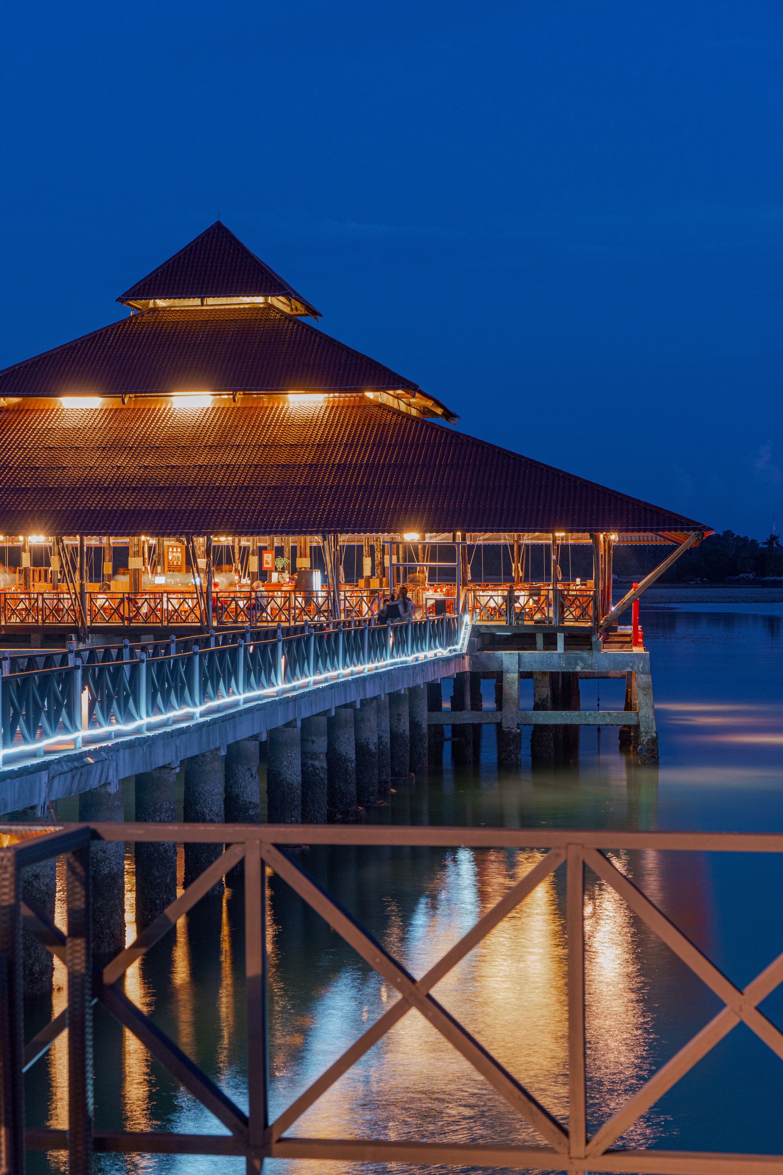 A waterfront restaurant with a covered dining area, a long deck, and a view of the water.