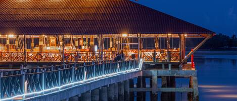 A waterfront restaurant with a covered dining area, a long deck, and a view of the water.