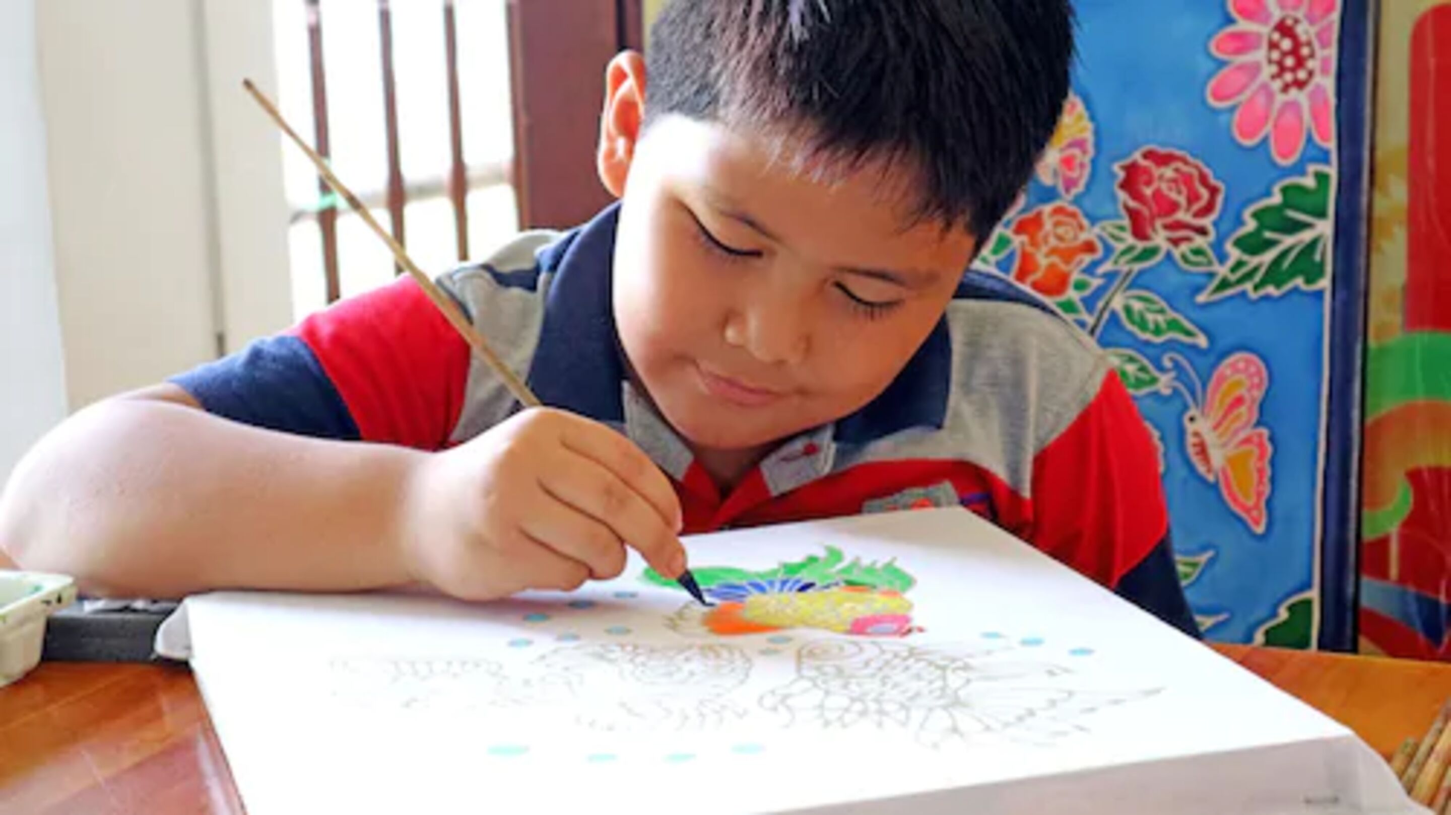 Un niño pintando sobre un papel con un fondo colorido.