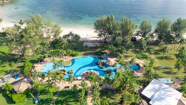 A resort with a large swimming pool, palm trees, and a beach.