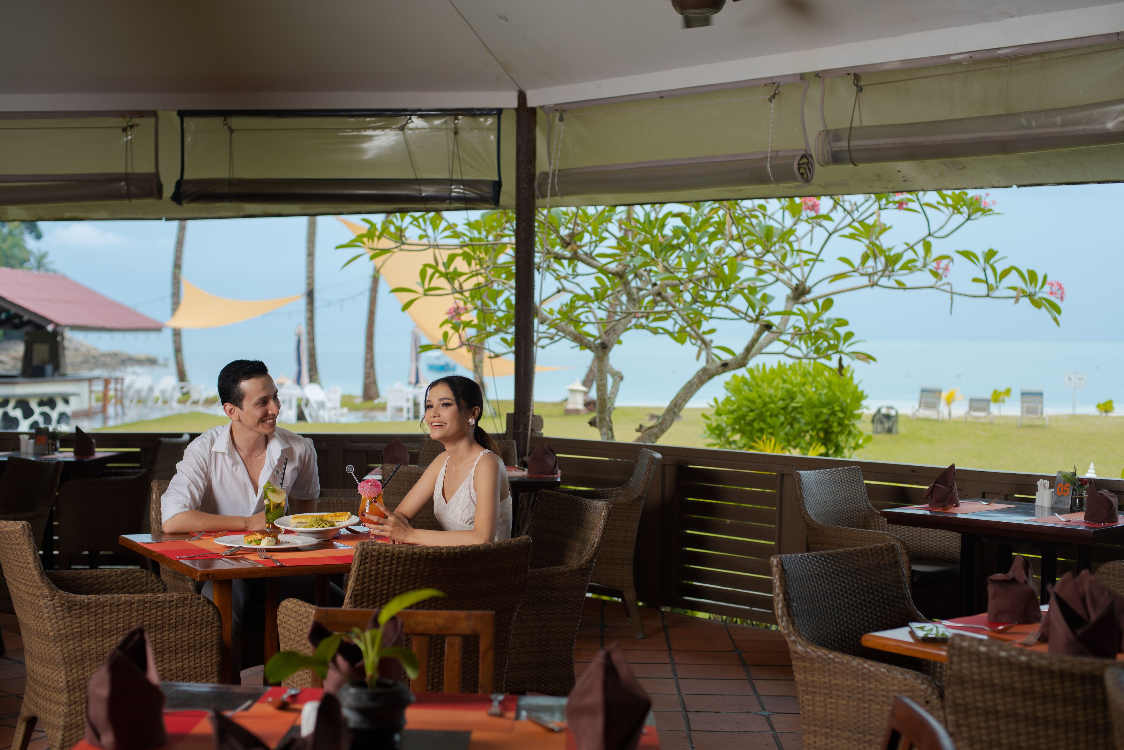 A restaurant with wicker furniture, outdoor seating, and a view of the beach.
